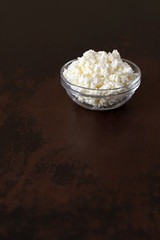 Cottage cheese crumbly in a glass bowl on a wooden old brown tabletop