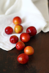 Plum fruit red orange scattered on wooden old brown tabletop and beige crumpled tablecloth.