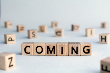 Coming - word from wooden blocks with letters,  to move or or change or happen announce concept, random letters around, top view on wooden background