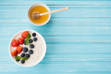 Healthy Breakfast of oatmeal with fresh strawberries, blueberries and honey on a blue background. Copy space