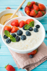 Healthy Breakfast of oatmeal with fresh strawberries, blueberries and honey on a blue background.