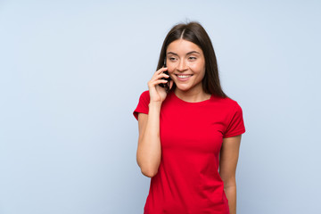 Brunette young woman with a mobile phone over isolated blue wall