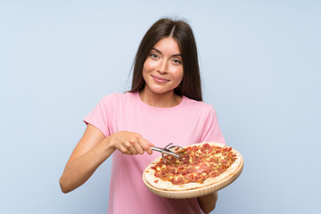 Pretty young girl holding a pizza over isolated blue wall