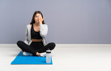 Fototapeta premium Young sport woman sitting on the floor with mat covering a eye by hand