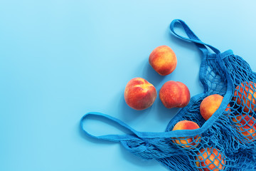 Ripe fresh peaches in a mesh cotton bag on a blue background. Flat lay, top view, copy space