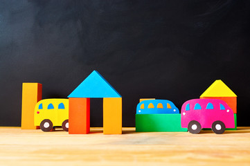 Cars cut out of paper and houses from cubes on a black background. Educational toys for preschool...
