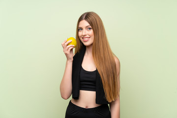 Young sport woman over isolated green background with an apple