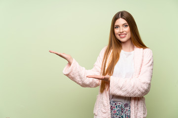 Young woman in dressing gown over green wall extending hands to the side for inviting to come