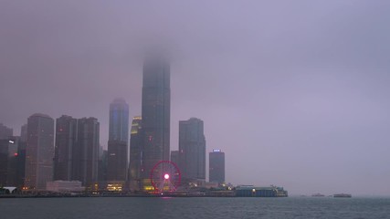 Time lapse day to night of Hong Kong cityscape with hard mist at the harbor in the raining day