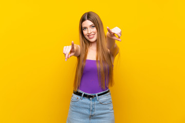 Young woman over isolated yellow background points finger at you while smiling