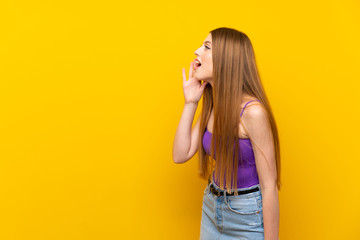 Young woman over isolated yellow background shouting with mouth wide open to the lateral
