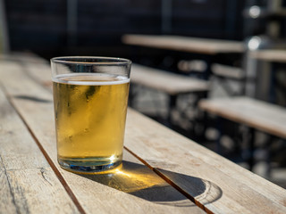 Short glass of blond beer sitting on outdoor table during summer day'
