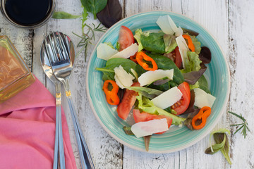 Home made fresh salad with parmezan cheese, greens and tomato. White rustic wooden table. Top view.