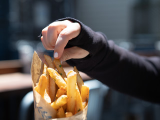 Woman in long sleeve black shirt taking crispy French fry on bright day