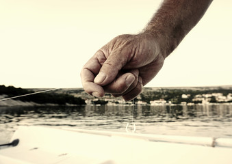 Obraz premium Hand and arm of an old fisherman holding a fishing thread and fishing fish in the sea