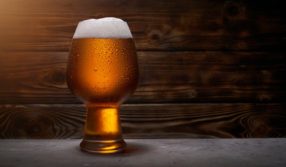 Glass of golden beer over wooden background with copy space