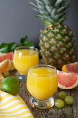Pineapple cocktail or juice in glass jar bottle with straws and fruits on background - pineapple, oranges, grapefruit, lime and grapes. Gray background. Summer cold drink.