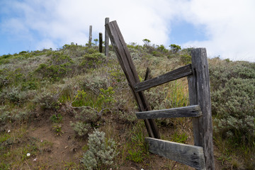Broken and rustic wooden fence sitting on grassy hill in hike trail