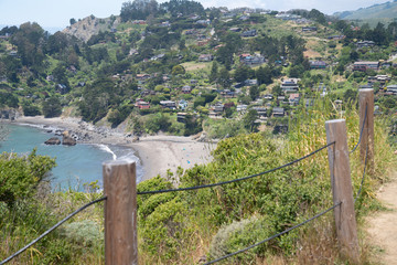 Fototapeta na wymiar Wooden and wire fence with beach town with houses on hill next to ocean
