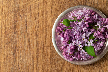 Obraz na płótnie Canvas Lilac flowers on a silver plate on a wooden background