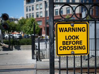 Warning look before crossing yellow warning sign at train crossing in city