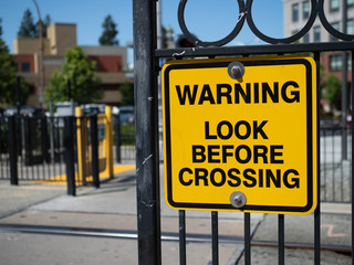 Obraz premium Warning look before crossing yellow warning sign at train station