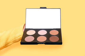 Eyeshadows and correctors, a large palette of make-up artist in hand over yellow background. . Makeup Accessories