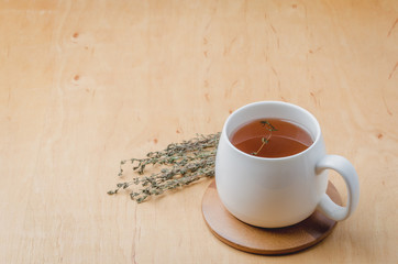 Thyme herbal tea in a white cup on a wooden table. Space for a text
