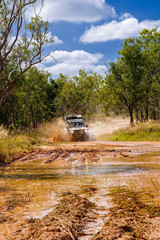 Fototapeta premium Western Australia – Flooded Outback gravel road with 4WD car crossing the waterhole with splashing muddy water at the savanna