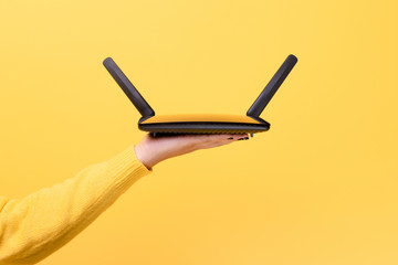 black wifi router on female hand over yellow background - obrazy, fototapety, plakaty