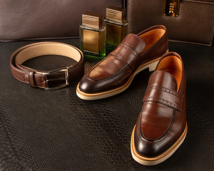 Set of brown men's shoes, waist belt and two bottles of men's perfume on the background of brown men's briefcases