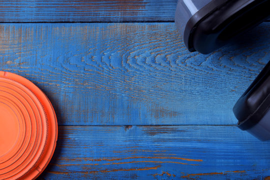 Flying target plate and noise suppression headphones against the blue wooden background. Copy space in the middle