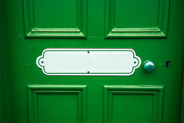 Old blank oval vintage metal painted sign with copy space on a painted green wooden background with matching door handle