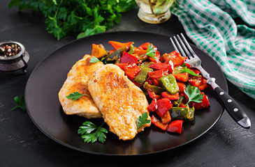 Grilled chicken fillets and sweet pepper on black plate.