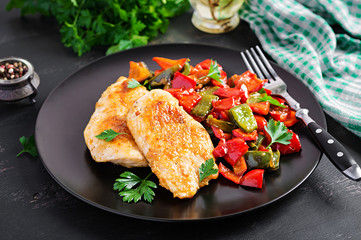 Grilled chicken fillets and sweet pepper on black plate.