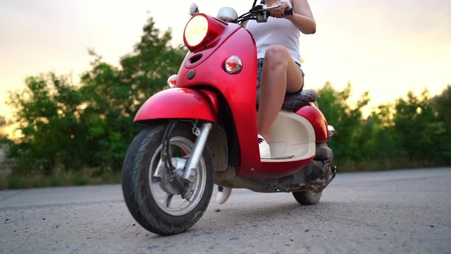 Pretty girl in helmet driving red scooter on countryside road. Travel, journey, freedom concept