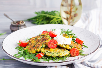 Zucchini pancakes with corn and sour cream served arugula, tomatoes salad.