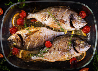 Baked fish dorado with lemon and herbs in baking pan on dark rustic background. Top view. Healthy dinner with fish concept. Dieting and clean eating