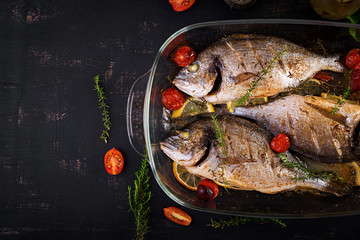 Baked fish dorado with lemon and herbs in baking pan on dark rustic background. Top view. Healthy...
