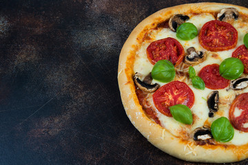 Pizza with tomatoes, cheese and mushrooms on a dark background with copy space