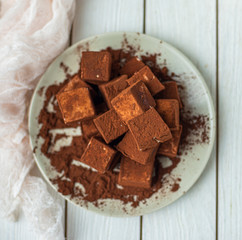 handmade souffle cubes covered with cocoa powder and pieces of chocolate lie on a plate on a light wooden table.
