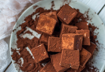 handmade souffle cubes covered with cocoa powder and pieces of chocolate lie on a plate on a light wooden table.