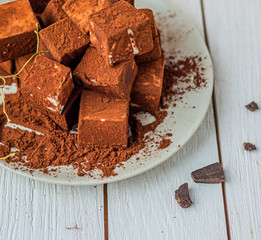 handmade souffle cubes covered with cocoa powder and pieces of chocolate lie on a plate on a light wooden table.