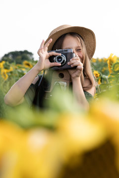Little girl blogger in the sunflowers. In a hat and a beautiful dress. Holding a vintage photo camera in his hands and taking pictures