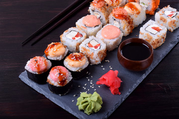 Sushi rolls assortment, wasabi, marinated ginger and soy sauce served on slate plate on black table