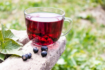 Glass cup of fruit tea with black currant berries on a wooden table in the open air. Close-up.