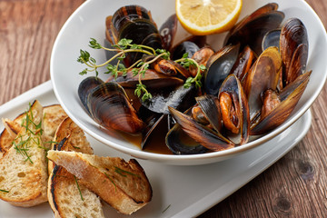 Mussels on a white plate on a wooden board