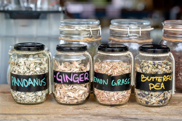 Assortment of dried spices in glass bottles on wooden background. Dry ginger, pandanus, lemon grass and butterfly pea in glass jars