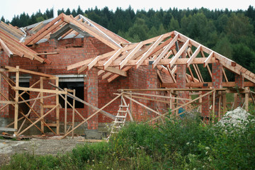 Building a house of red brick. Mounting the roof from wooden boards.