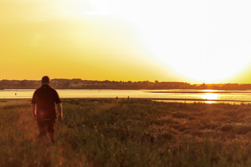 20 something male walking away from the camera towards the sunset on a warm summers evening on the Suffolk coast